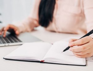 A person writing notes in a notebook while using a laptop for RTO training.