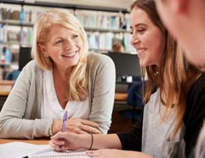 A teacher helps students with their studies in a library, highlighting the importance of student welfare in VET.