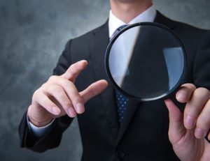 A businessman uses a magnifying glass to review assessment evidence for thorough vet compliance.